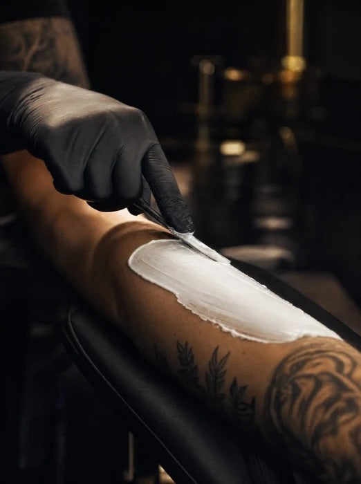 Spreading a thick even layer of numbing cream along a forearm with a spatula